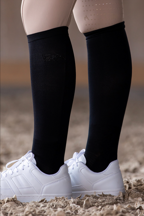Person, die schwarze EquiAttire-Reitsocken und weiße Turnschuhe trägt.